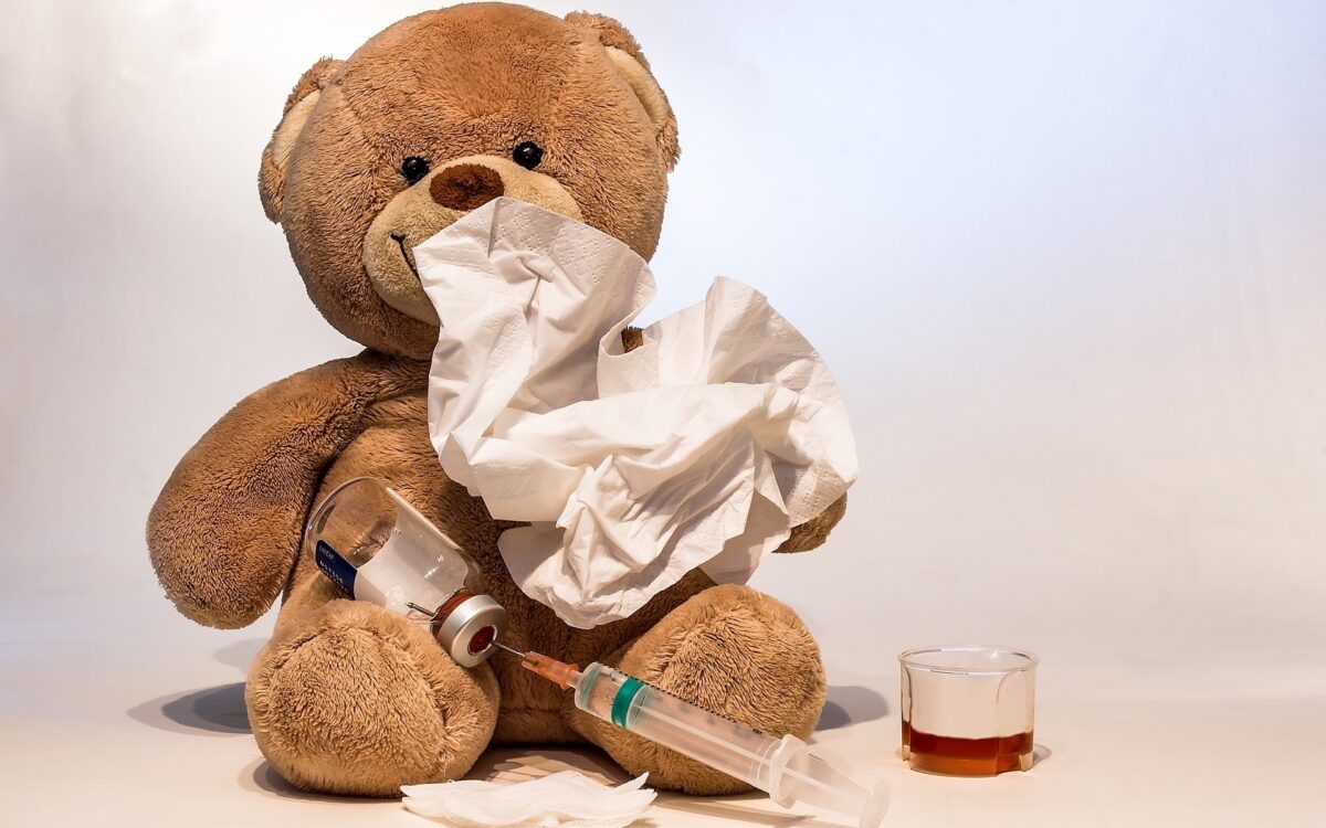 Ein Teddy sitzt mit Taschentuch, Grippeimpfung und Medizin auf dem Boden Ein Teddy sitzt mit Taschentuch, Grippeimpfung und Medizin auf dem Boden
